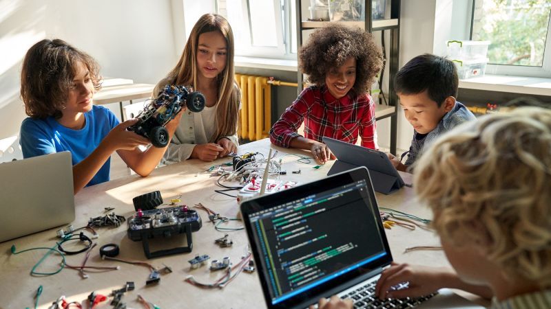 Kinder an einem Tisch voller Laptops und Kabeln/elektronischem Zubehör