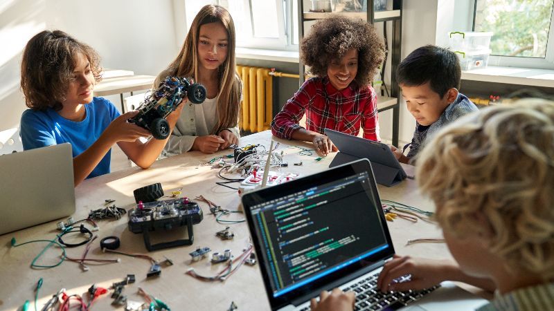 Kinder an einem Tisch voller Laptops und Kabeln/elektronischem Zubehör