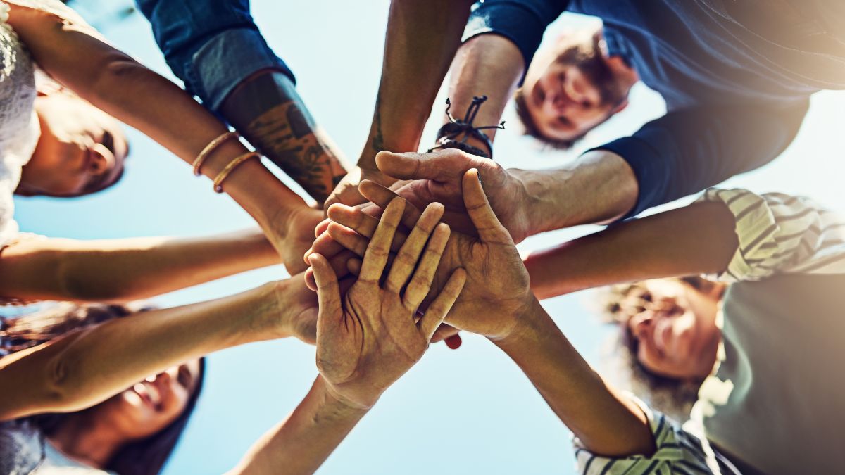 Gruppe verschiedener Menschen legt gemeinsam die Hände übereinander – Symbol für Teamarbeit, Zusammenhalt und Gemeinschaft.