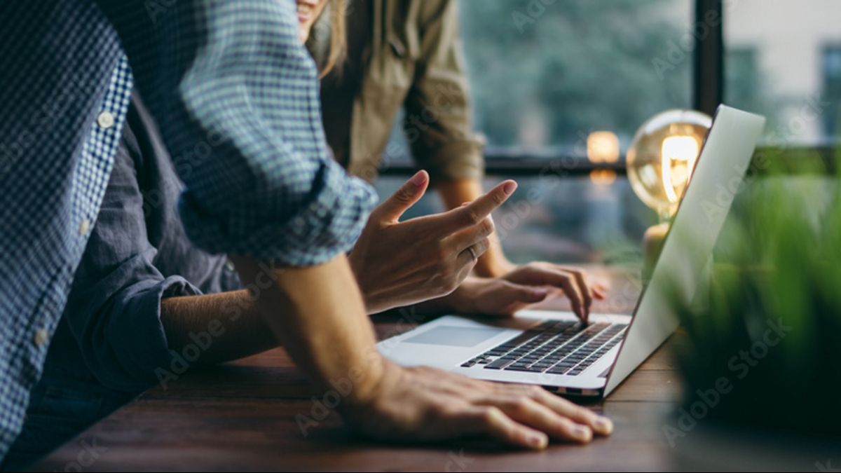 Keyvisual der IN.NRW: Zwei Menschen stehen an einem Holztisch und beugen sich über einen Laptop.