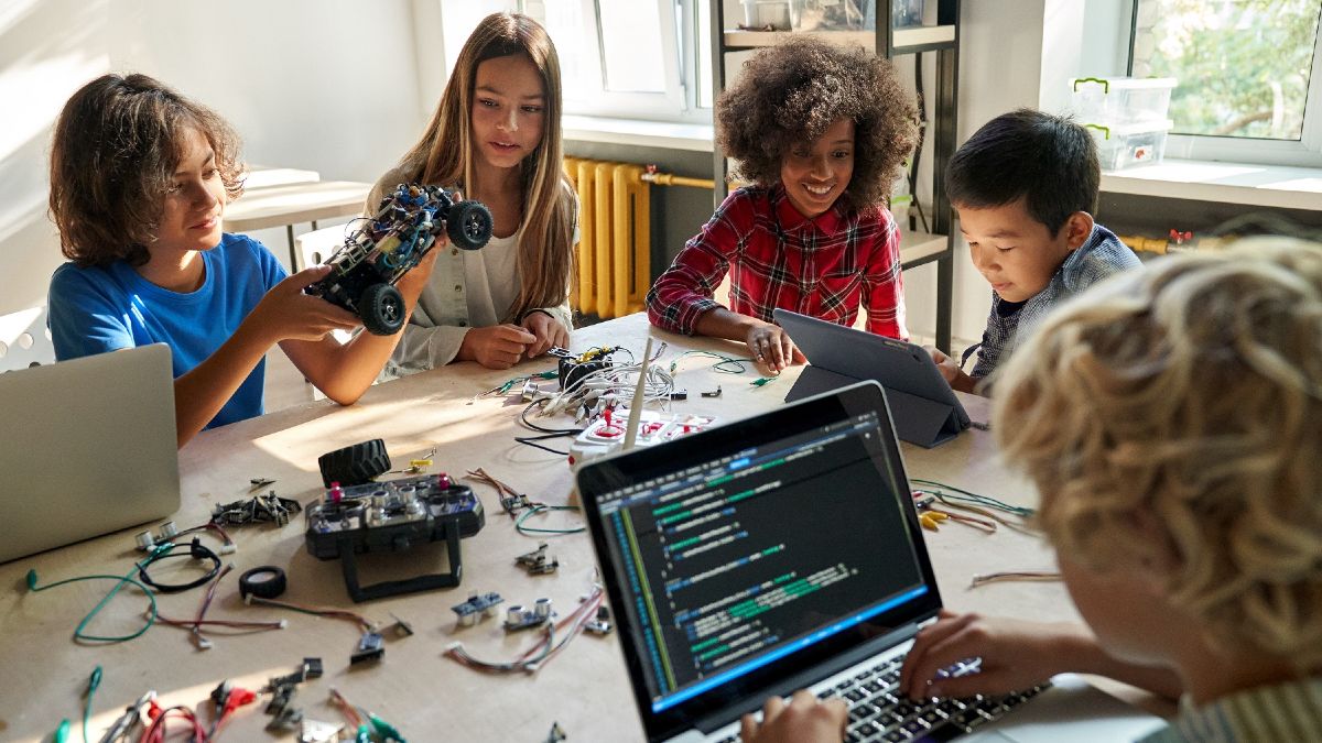 Schulkinder arbeiten an einem Gruppentisch mit Laptops und Konstruktionsmaterialien.