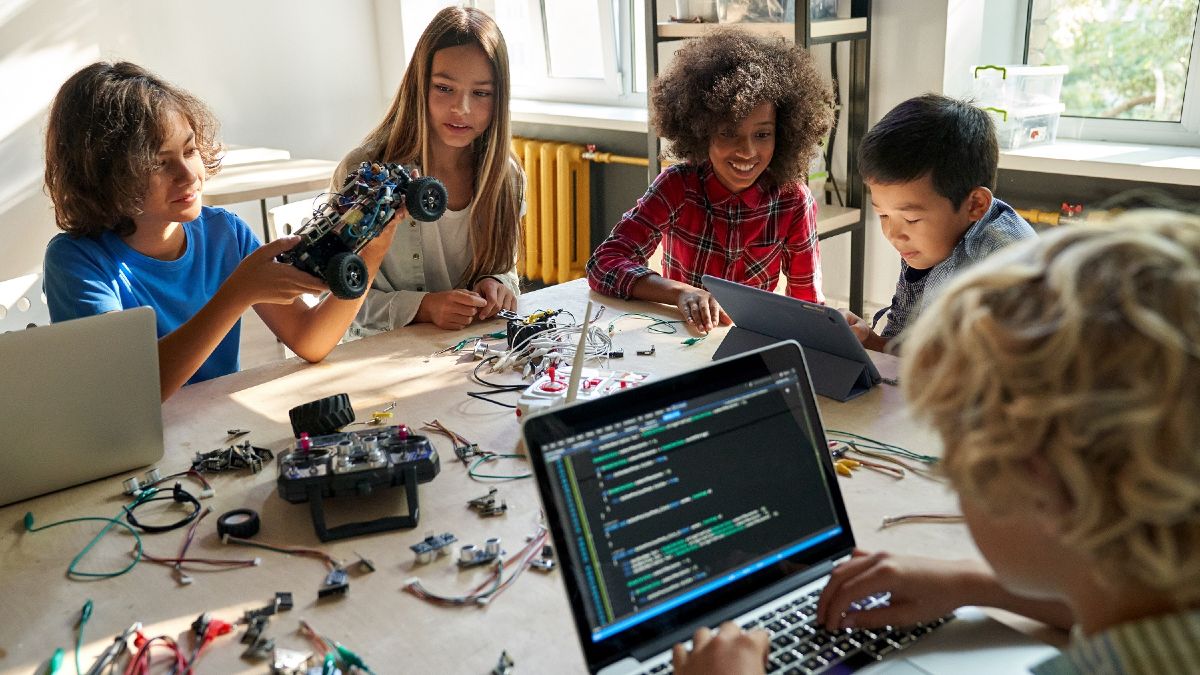 Kinder an einem Tisch voller Laptops und Kabeln/elektronischem Zubehör